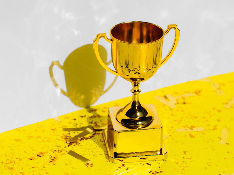 Golden champions cup standing on yellow background with glitter and confetti. Trendy colors of 2021 year