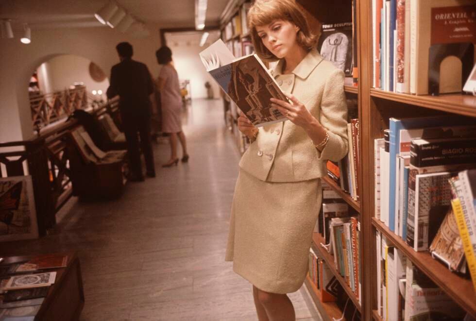 An unidentified model in a cream suit leans against a bookcase as she reads a book on Egyptian art in the Rizzoli bookstore (at 712 5th Avenue), New York, New York, December 1964. The photo was part of a fashion shoot for Glamour Magazine. (Photo by Susuan Wood/Getty Images)